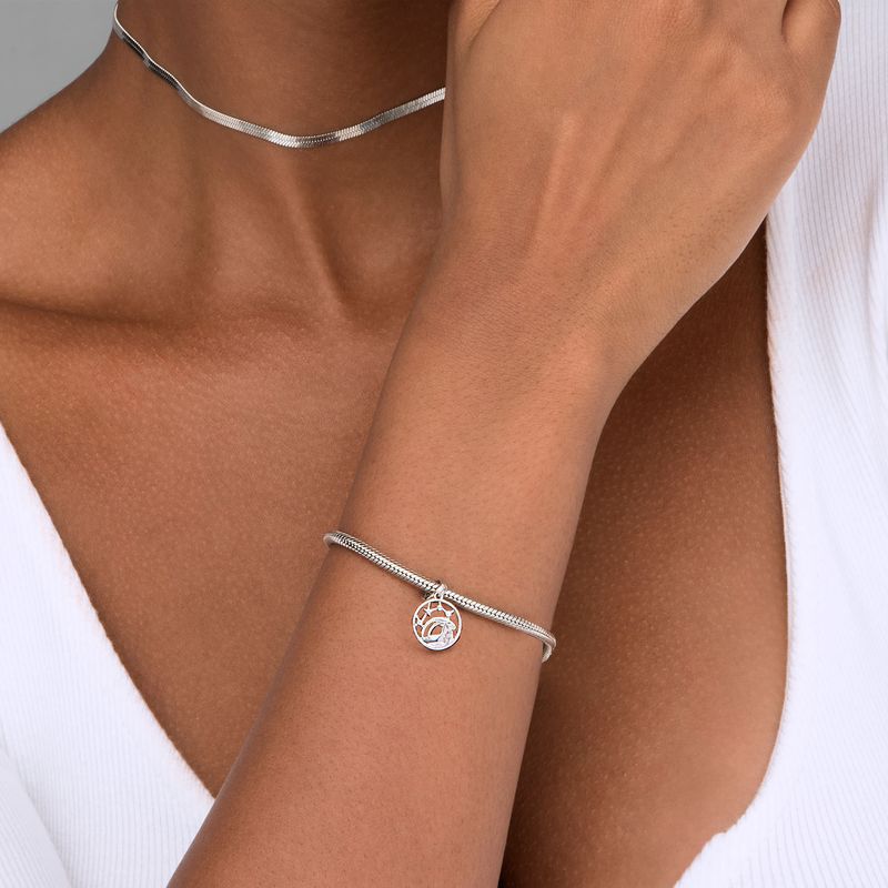 Pulsera de prata com pingente de árvore da vida, usada no braço de uma pessoa com pele morena, vestindo uma camisa branca.