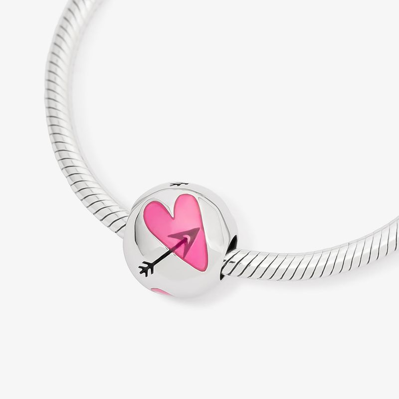 Pingente de metal prateado com coração rosa e flecha preta no centro, preso a uma corrente de metal prateado.