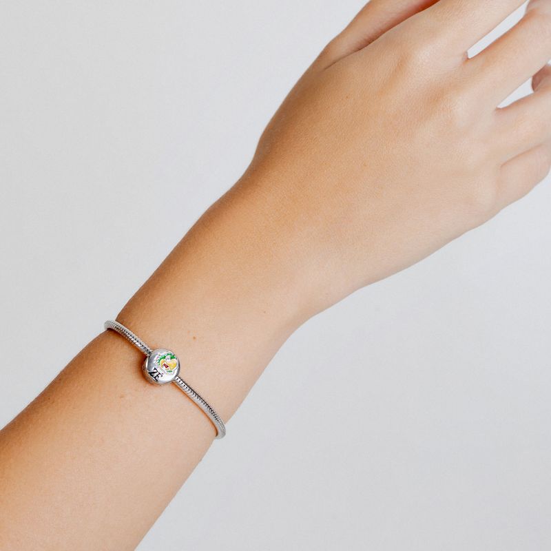 Pulseira prateada com pingente de coração colorido, ajustada ao pulso de uma mão.