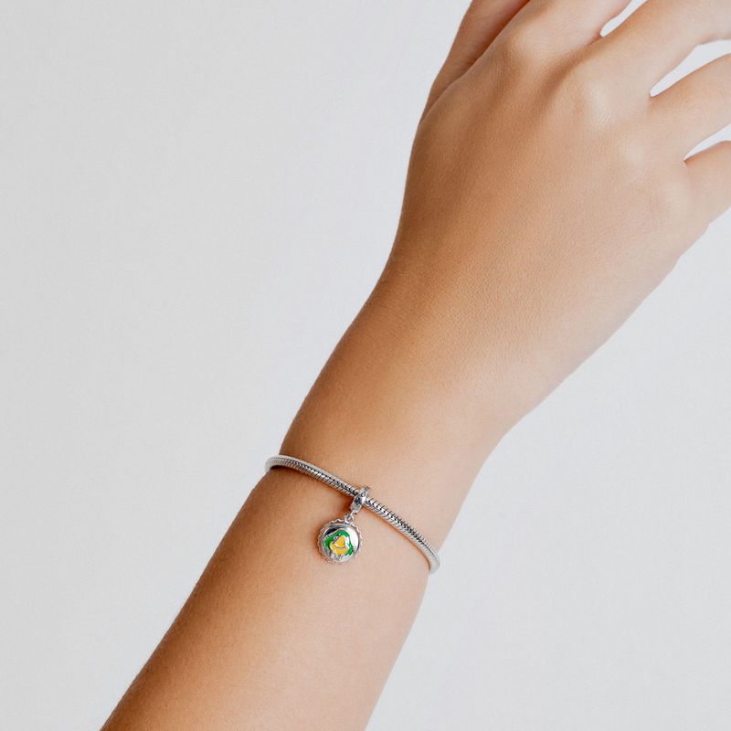 Pulseira de prata com pingente circular decorado com o símbolo da paz em cores verde, amarelo e branco, usada no pulso de uma pessoa.