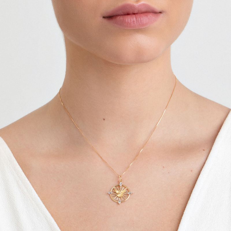 Colar dourado com pingente de sol e detalhes em pedras transparentes, usado por uma pessoa com pele clara e vestindo blusa branca.
