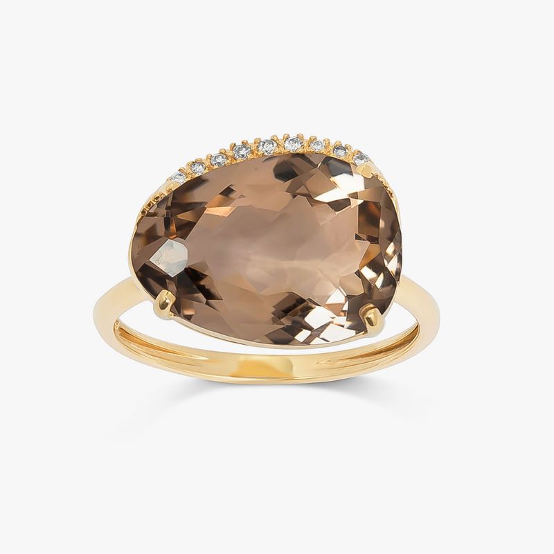 Anel com acabamento dourado, contendo uma pedra grande oval de cor marrom escura e detalhes de pedras menores ao redor.