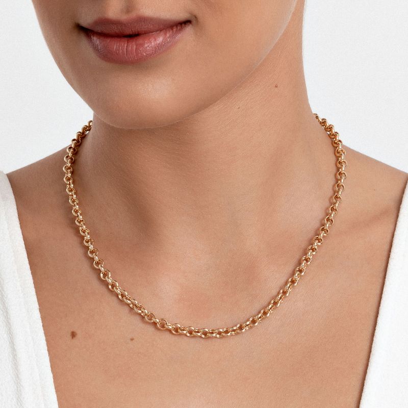 Colar dourado de elos grossos, usado por uma pessoa que veste roupa branca.