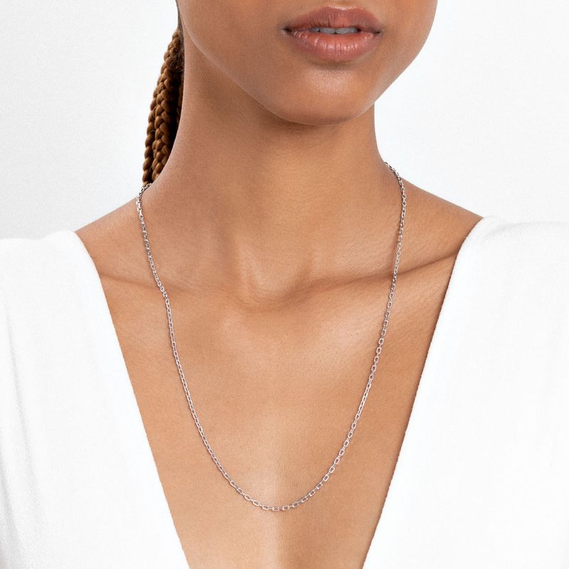 Colar delicado de corrente prateada sendo usado por mulher com pele morena clara, usando roupa branca de decote V.