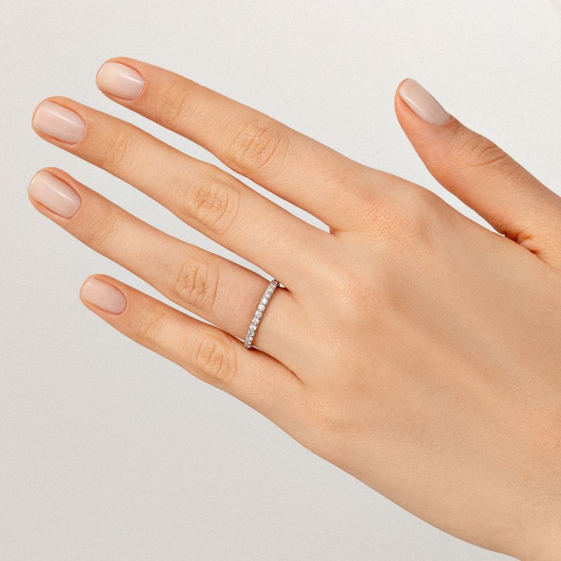 Mão com unhas nude e um anel com pedras brilhantes na dedo médio.