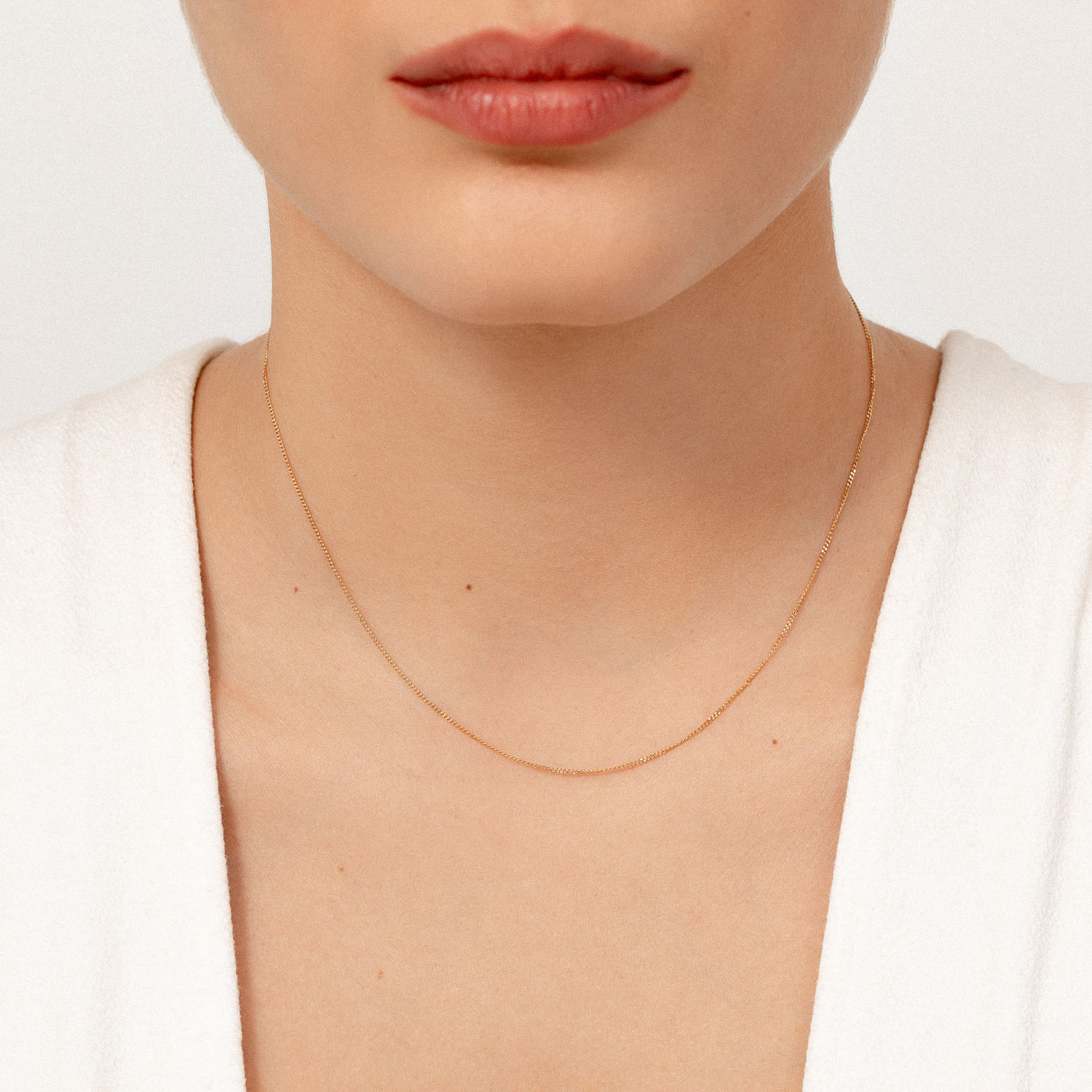 Colar delicado de corrente dourada ao redor do pescoço de uma mulher com pele clara, usando uma blusa branca.