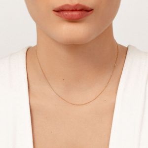 Colar delicado de corrente dourada ao redor do pescoço de uma mulher com pele clara, usando uma blusa branca.