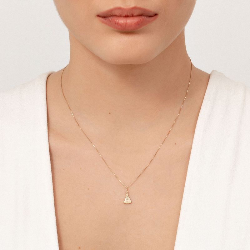 Colar dourado delicado com pingente de forma triangular, usado por uma mulher com pele clara e vestindo branco.
