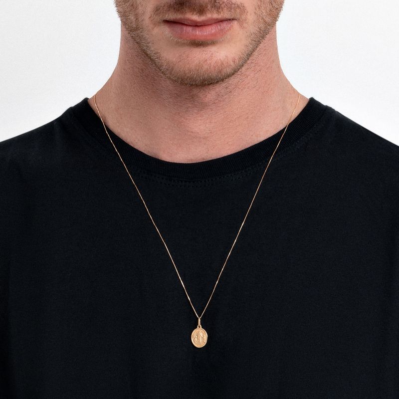 Colar dourado com pingente circular e medalha, vestido com camiseta preta.