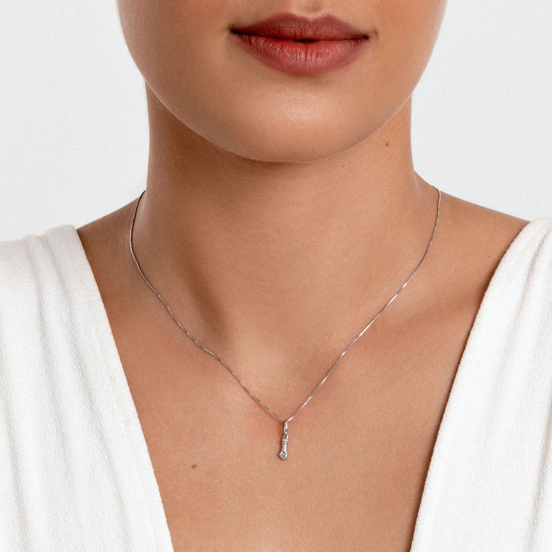 Colar delicado de prata com pingente em formato de gota, usado por uma mulher com pele clara e camisa branca.