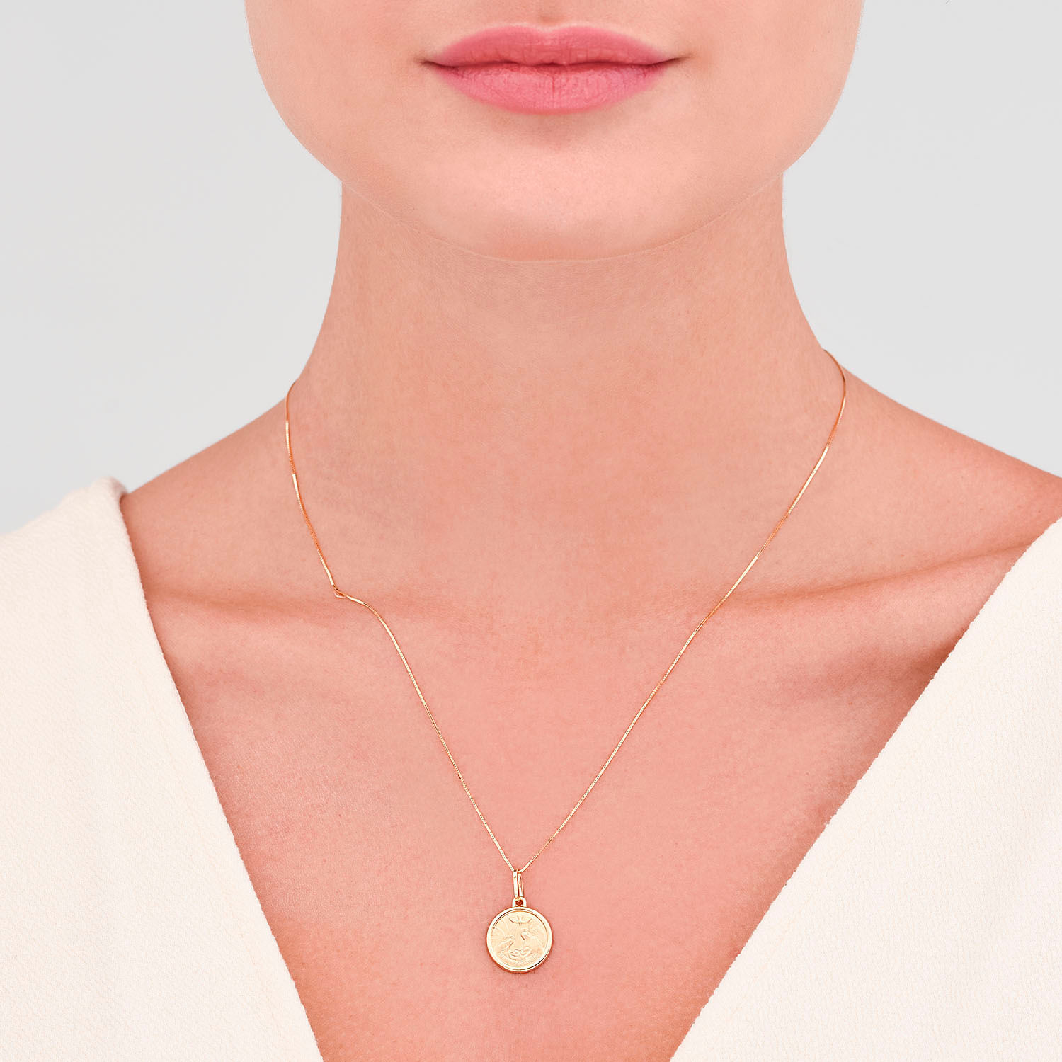 Colar delicado de corrente fina com pingente redondo dourado, usado na linha do pescoço de uma mulher com pele clara e lábios rosados.