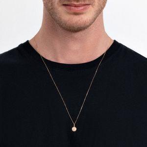 Colar delicado dourado com pingente circular, usado por um homem com camiseta preta.