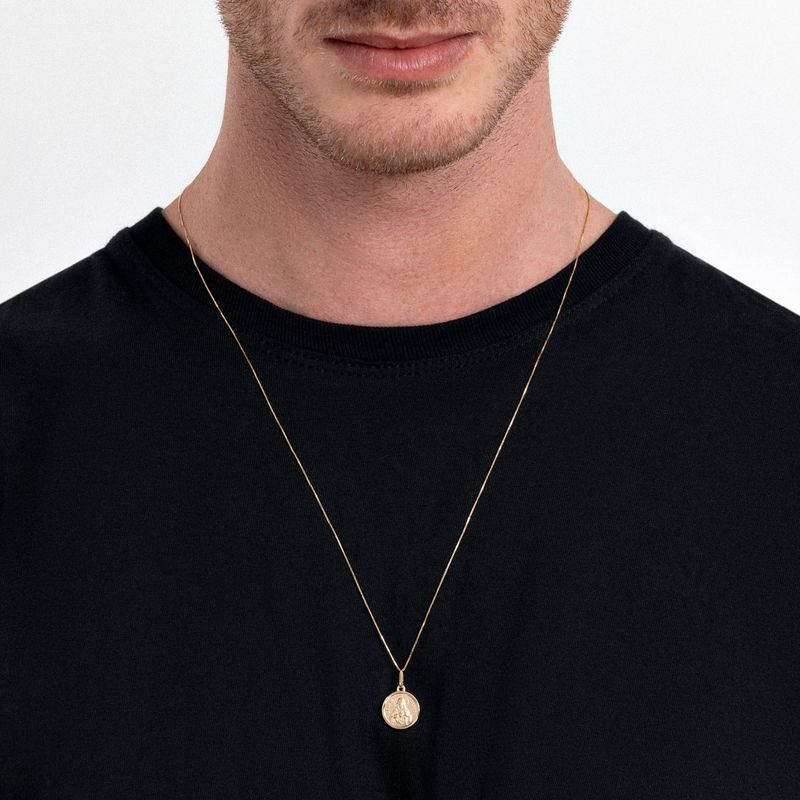 Colar dourado com pingente redondo, usado por um homem com camiseta preta.