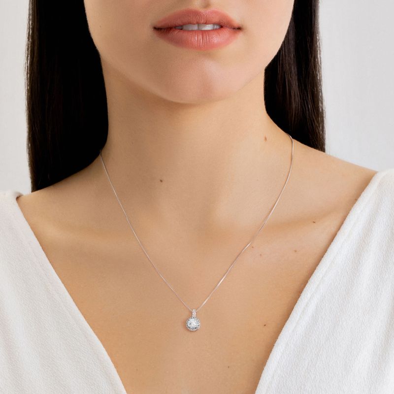 Colar delicado com pingente circular de pedras brilhantes, usado por uma mulher com roupa branca.