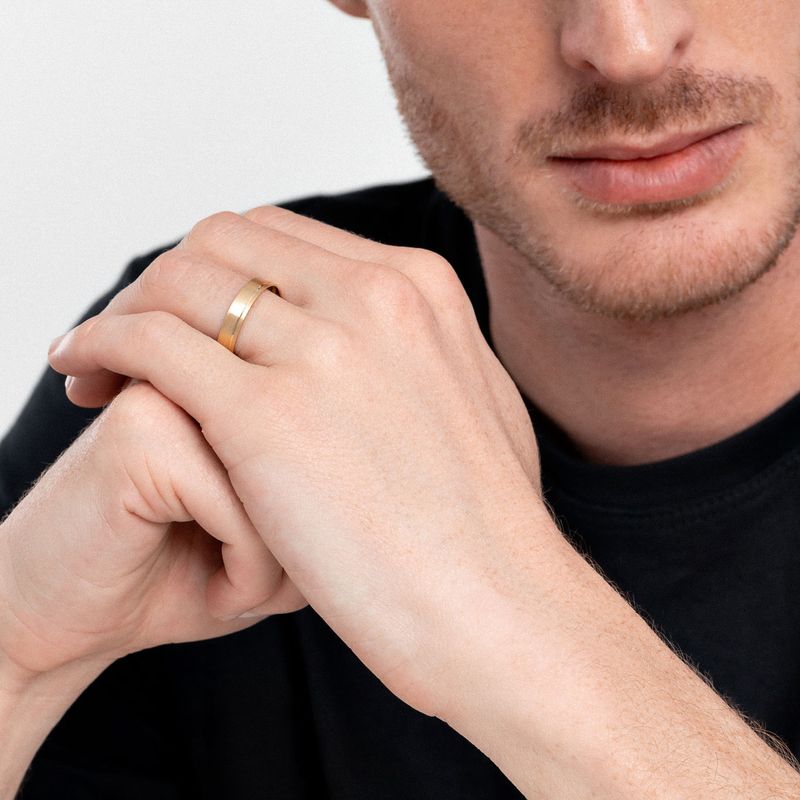 Mão de homem com barba, usando anel dourado na mão esquerda, apoiada no queixo, vestindo camiseta preta.