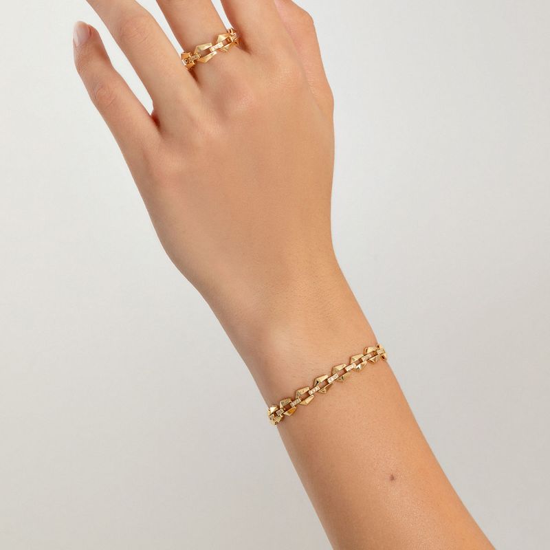 Pulseira dourada com elos facetados, usada no pulso de uma mão com anel dourado.