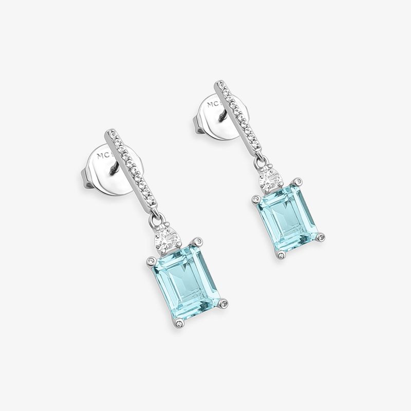 Par de brincos prateados com pedras quadradas de vidro azul claro e detalhes com pequenas pedras brilhantes.