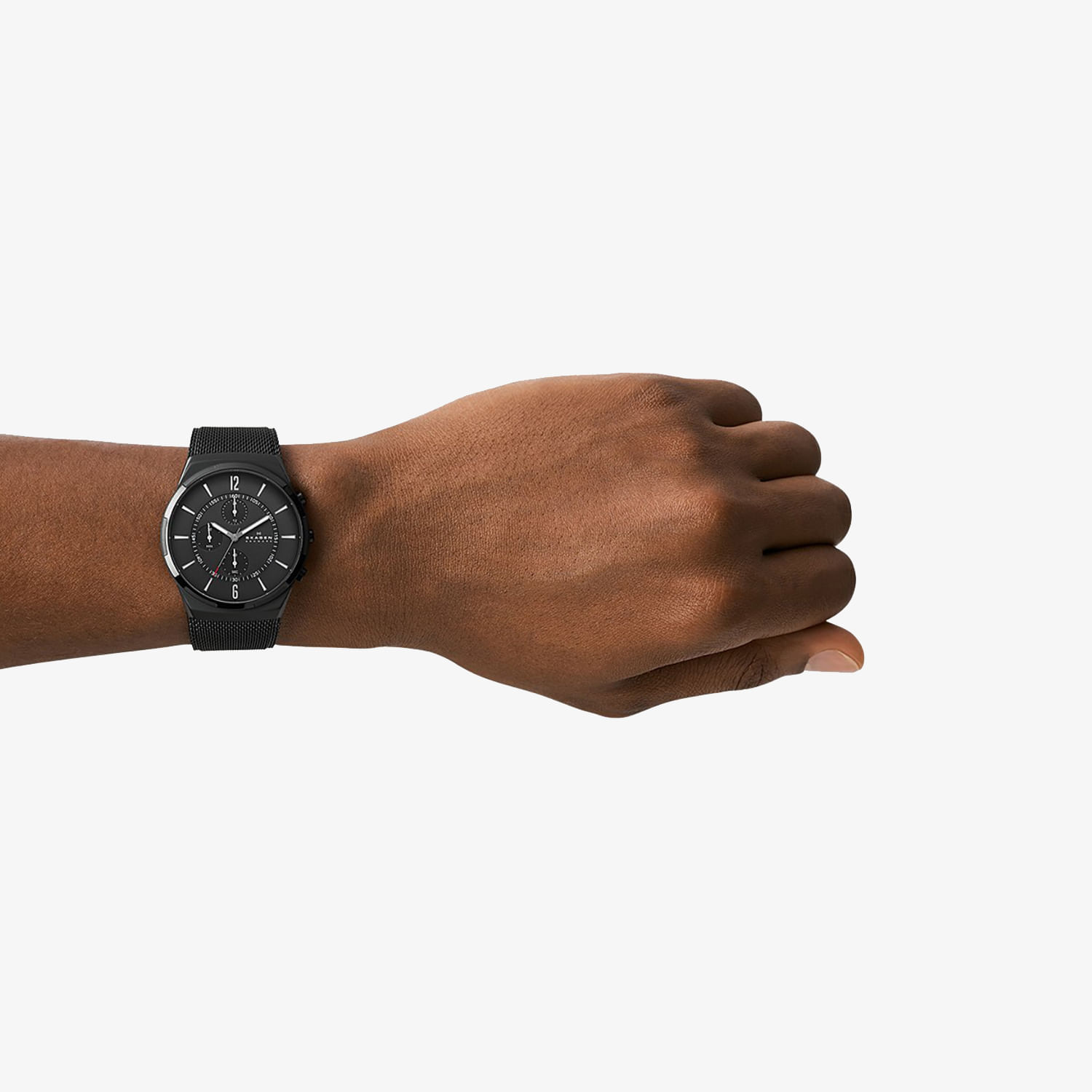Relógio preto com pulseira de malha metálica sendo exibido no pulso de uma pessoa de pele morena contra fundo branco.