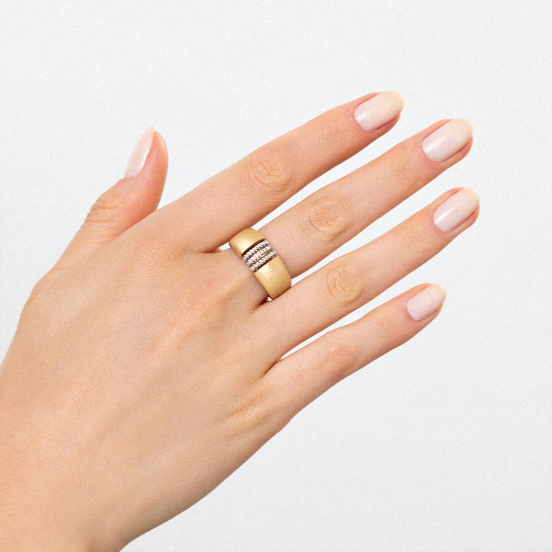 Mão com unhas naturais usando anel dourado com detalhes em pedras brancas na parte superior do dedo médio.