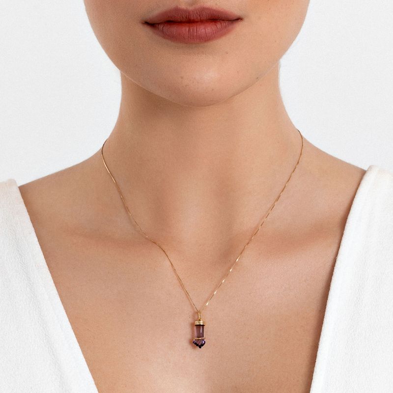 Colar delicado com pingente de pedra roxa, usado por uma mulher com roupas brancas.