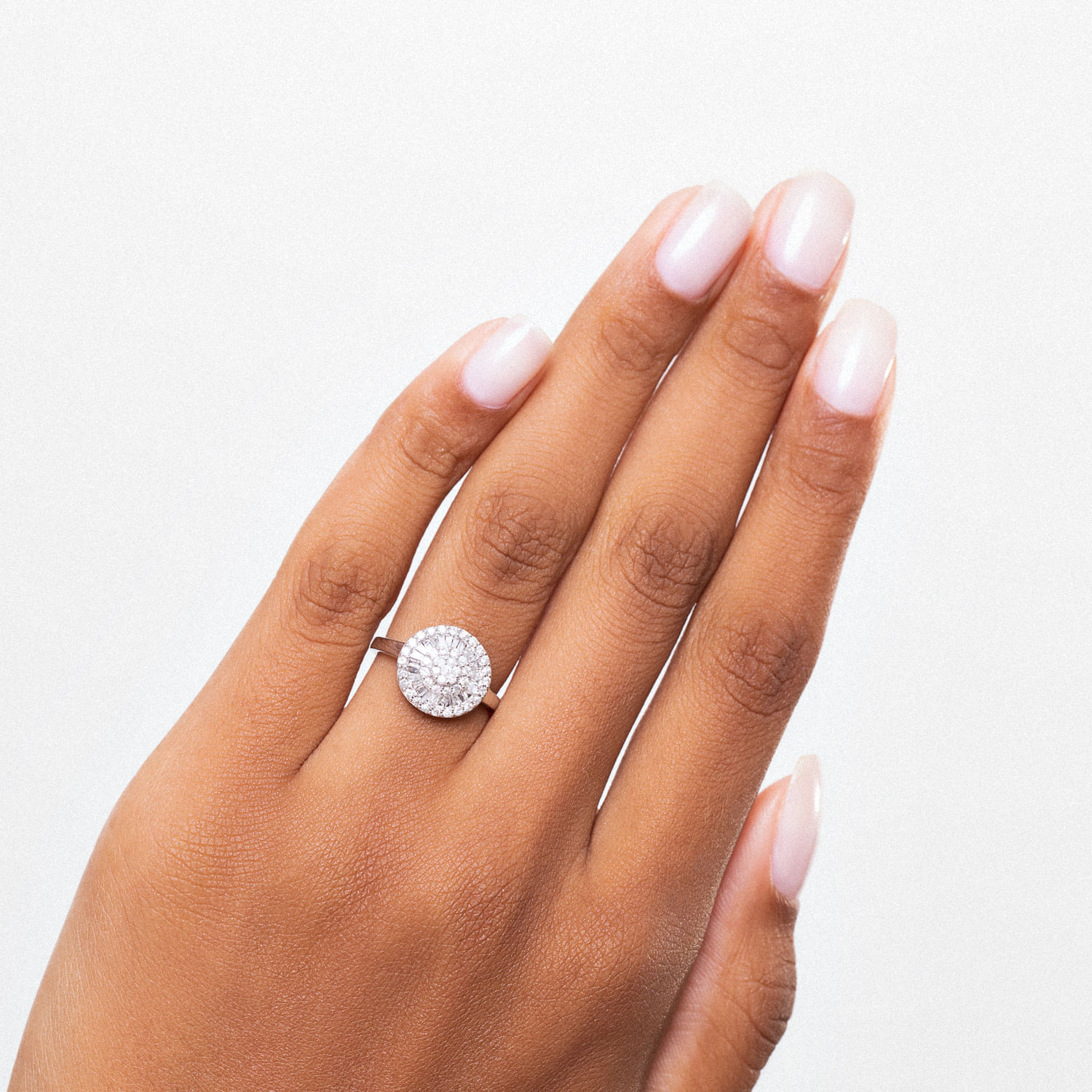 Dedo com esmalte claro e anel com grande pedra circular brilhante.