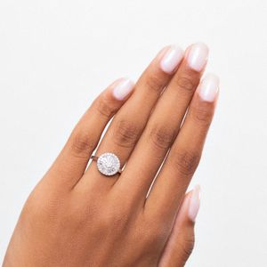 Dedo com esmalte claro e anel com grande pedra circular brilhante.