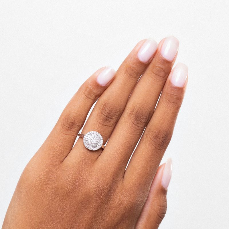 Dedo com esmalte claro e anel com grande pedra circular brilhante.