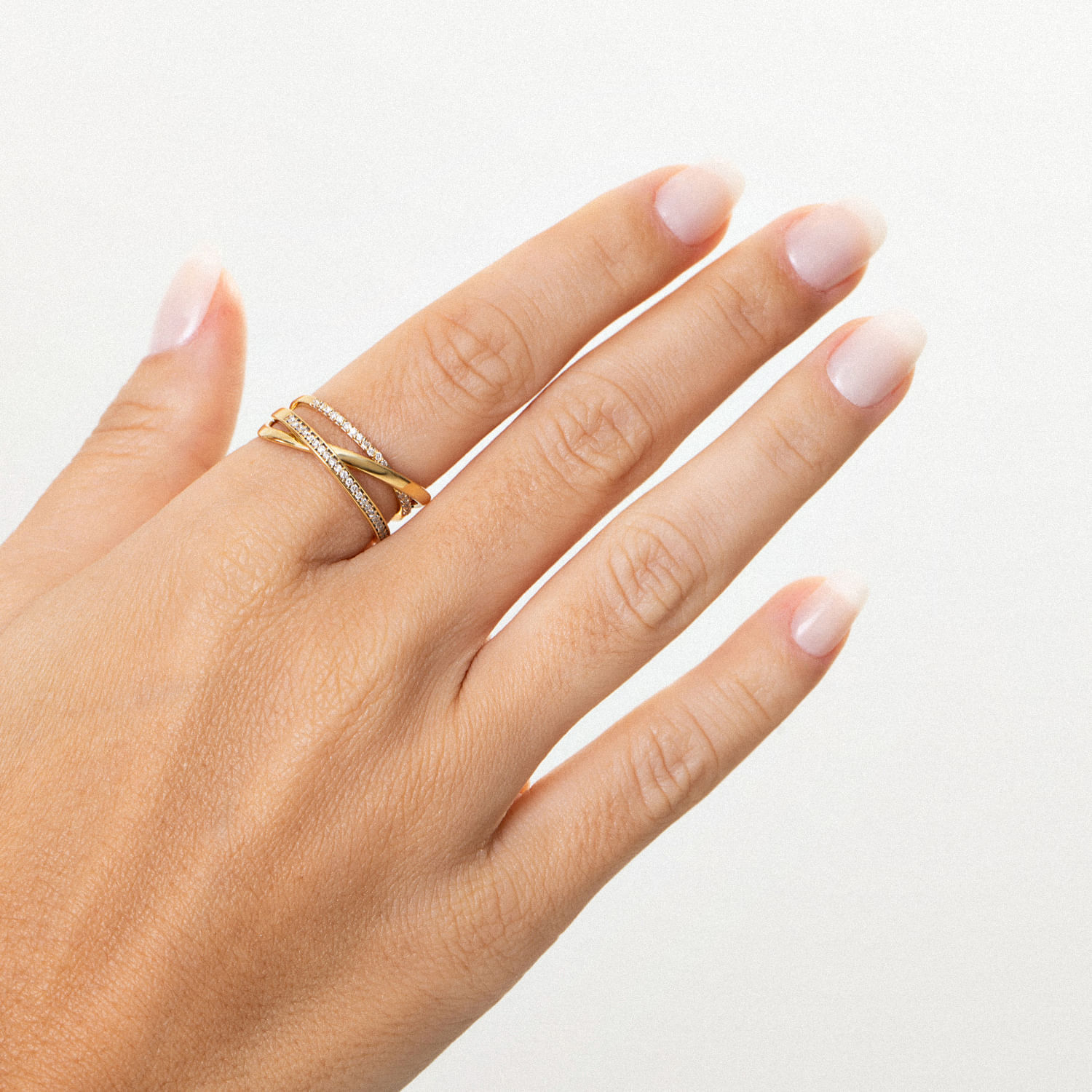 Dedo com várias alianças douradas, algumas com detalhes em pedras, sobre unhas naturally limpas e sem esmalte.