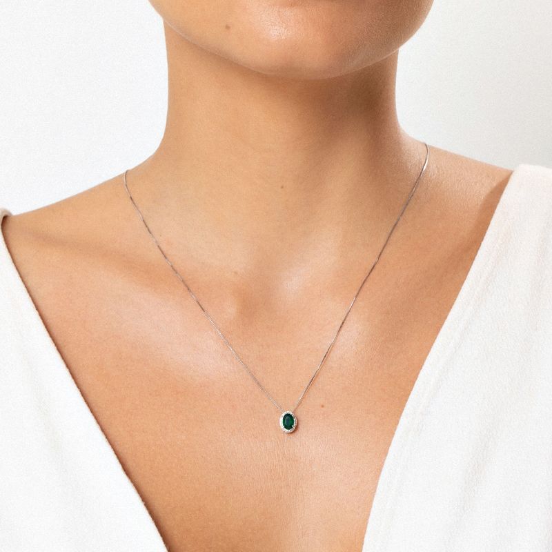 Colar com pingente de pedra verde em ouro branco, usado por uma pessoa com pele clara e roupa branca.