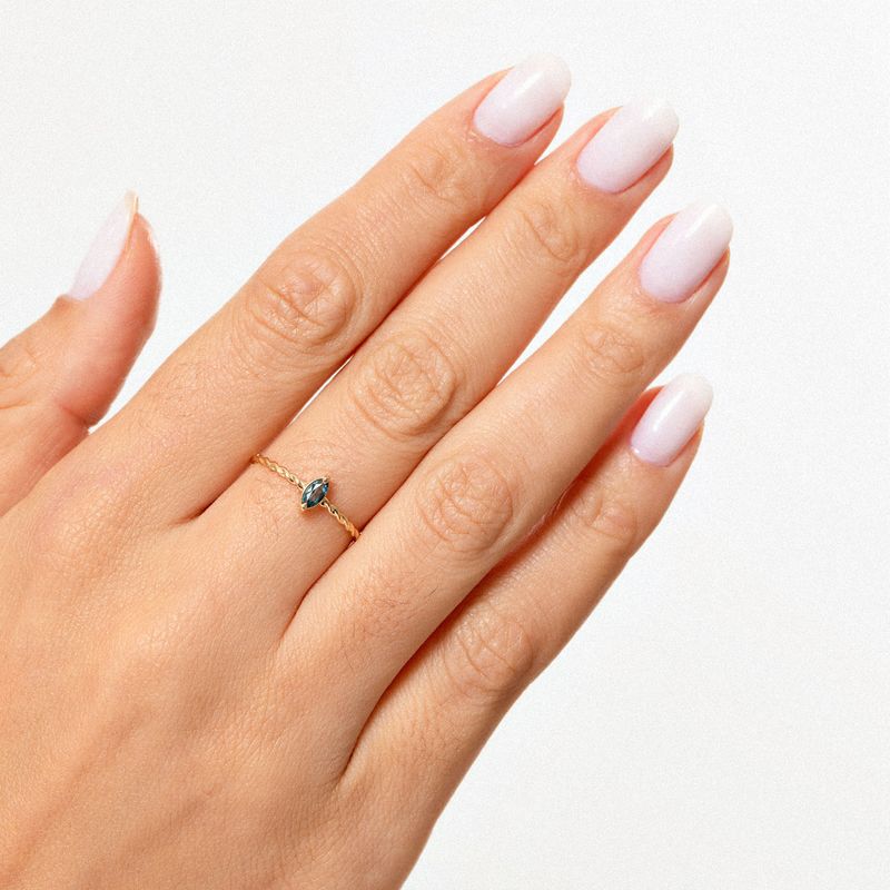 Dedo com unha bem cuidada usando esmalte branco, usando anel delicado com pedra azul em uma mão com pele clara.