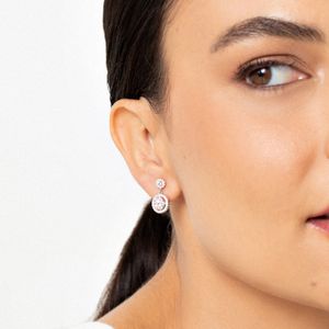 Close-up de uma mulher com brincos de diamante, mostrando apenas metade do rosto, cabelo castanho escuro e pele clara.