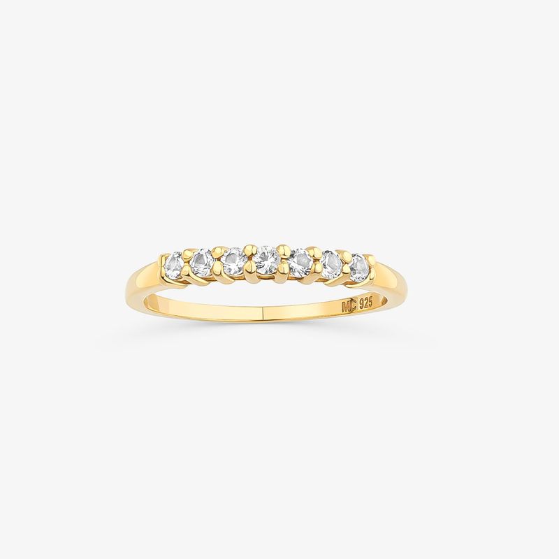 Anillo dourado com sete pedras de diamante alinhadas na parte superior.