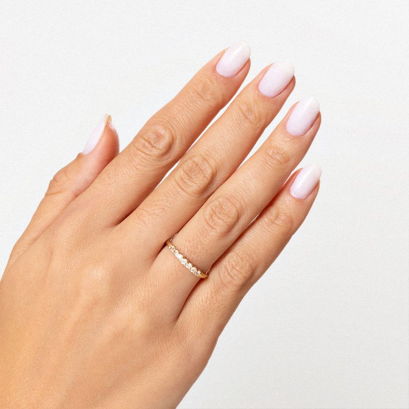 Mão com unha manicura francesa usando uma aliança de ouro com pequenas pedras brilhantes na roda.